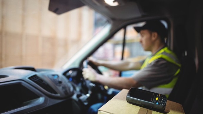 Delivery driver driving van with parcels on seat outside warehouse-2